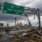 Damaged Interstate 10 East sign near downtown San Antonio after a tornado, with storm debris on the roadway and the Tower of the Americas visible in the background